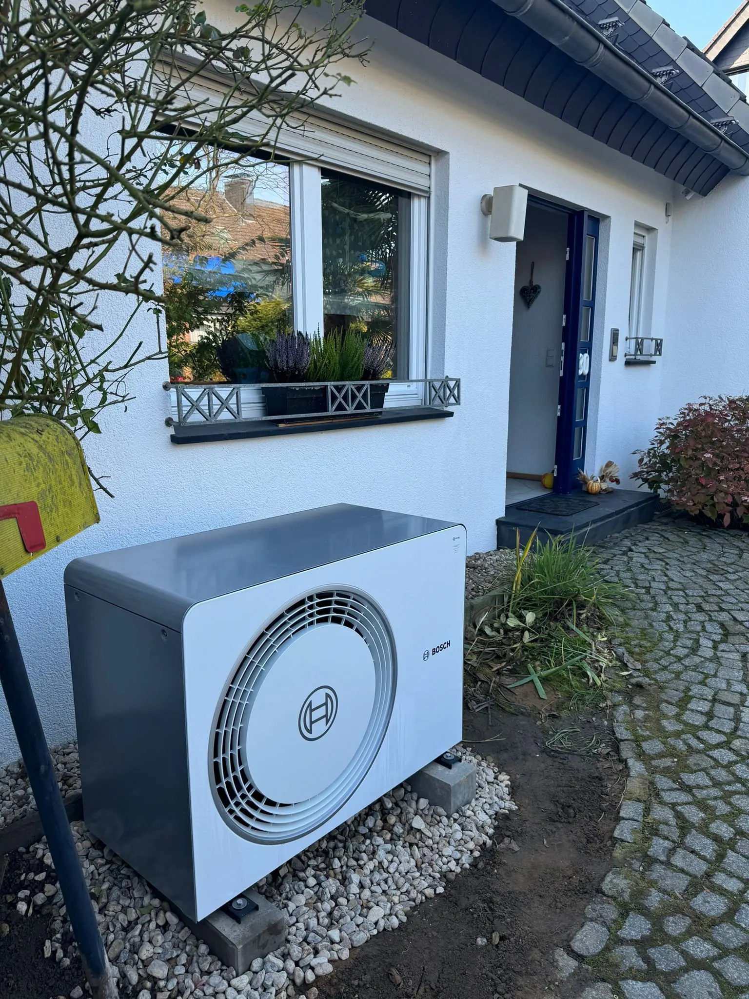 Außengerät einer Wärmepumpe vor einem Einfamilienhaus